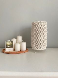 some white candles are sitting on a table next to a crocheted candle holder