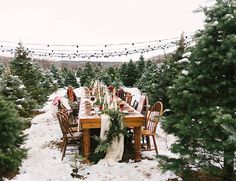 a table set up for christmas dinner in the middle of snowy woods with lights strung above