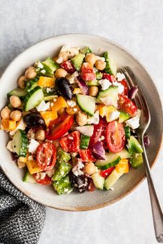 a white bowl filled with salad on top of a gray tablecloth next to a fork