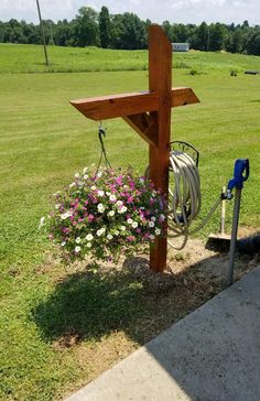 a wooden cross sitting on top of a lush green field next to a garden hose