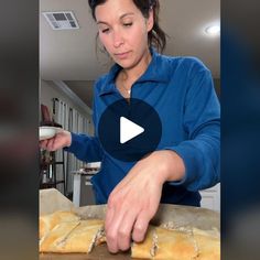 a woman in blue shirt making bread on top of a wooden table next to a white bowl