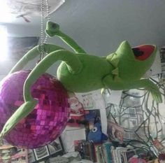 a green stuffed frog hanging from a ceiling with disco balls in it's mouth