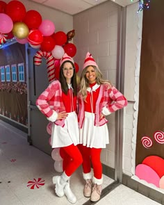 two women dressed in christmas costumes standing next to each other with balloons and candy canes behind them