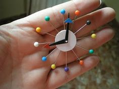 a hand holding a small clock with pins on it's face and multicolored nails