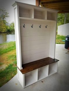 a white bench sitting under a wooden roof next to a body of water with hooks on it