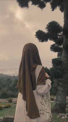 a woman in a brown and white robe is standing under a tree with her back to the camera