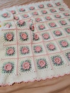 a crocheted blanket with pink flowers on it sitting on top of a bed