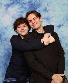 two young men hugging each other in front of a blue backdrop