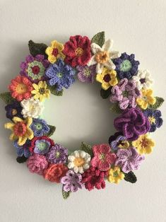 a crocheted wreath is hanging on the wall, with flowers in different colors