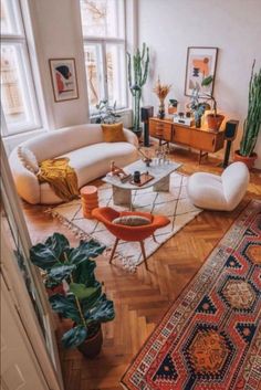 a living room filled with lots of furniture and plants on top of wooden flooring