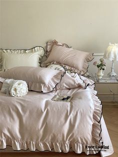 a bed with ruffled sheets and pillows on top of it, next to a lamp