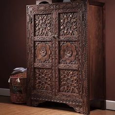 an ornate wooden armoire with carvings on the front and sides, sitting against a brown wall