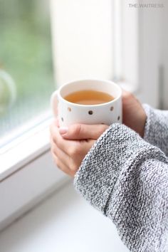 a woman holding a cup of tea in front of a window