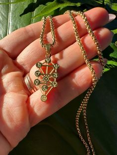 a hand holding a gold necklace with an ornate design on it