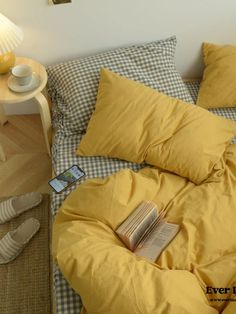 a bed with yellow sheets and pillows on top of it next to a night stand