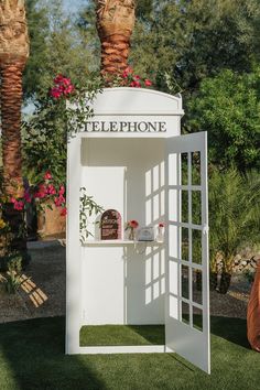 a white phone booth sitting on top of a lush green field next to palm trees