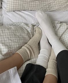 two people are laying in bed with their feet up on the covers and one is wearing socks