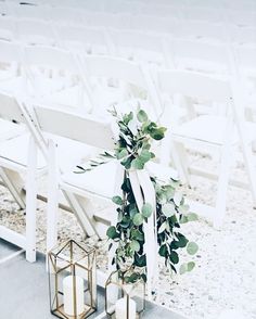 a bunch of white chairs sitting next to each other with greenery on top of them