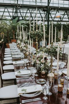 a long table is set with place settings and candles for an elegant wedding reception in a greenhouse