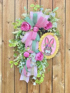 a wreath with pink roses, green leaves and an easter bunny on it hanging on a wooden fence