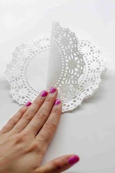 a woman's hand with pink nail polish holding a piece of white doily