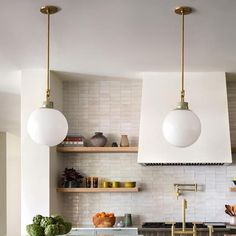 a kitchen with two hanging lights above the sink and counter top, surrounded by open shelving