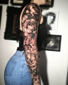 a woman with a black and white flower sleeve tattoo on her left arm, in front of a wall