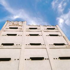 the side of a tall building with holes in it's windows and sky background