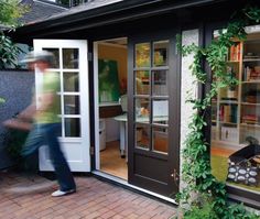 a man walking into a room with lots of plants on the outside wall and doors