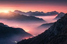 the sun is setting over mountains with fog in the valleys and low lying clouds below