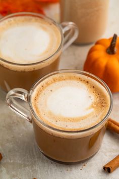 two mugs of hot chocolate with cinnamon sticks and pumpkins in the back ground