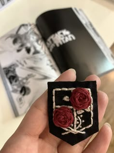 a hand holding a black and red brooch with two roses on it