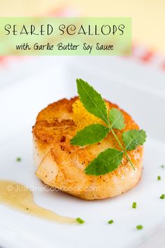 seared scallops with garlic butter soy sauce on a white plate, garnished with green leaves