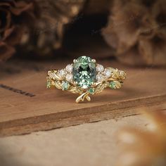 a green and white diamond ring sitting on top of a wooden table next to other jewelry items