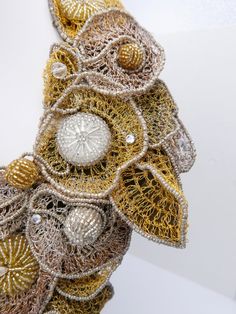 an intricate gold and silver piece with beads on it's side, sitting on a white surface