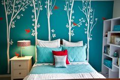 a bedroom with blue walls and white trees painted on the wall behind the headboard