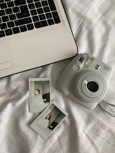 an open laptop computer sitting on top of a bed next to a polaroid camera