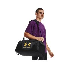 a man carrying a duffel bag with the under armour logo on it, in front of a white background