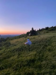 two people standing on top of a lush green hillside next to a forest at sunset