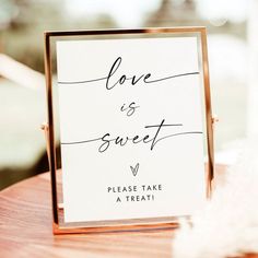 a sign that says love is sweet on top of a wooden table next to feathers