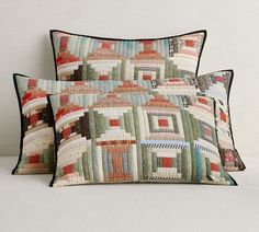 two decorative pillows sitting next to each other on a white surface with a wall in the background