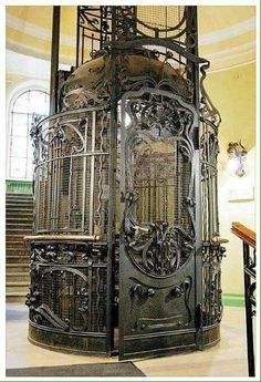 an ornate metal structure in the center of a building with stairs and windows behind it