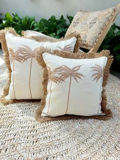 three pillows with palm trees on them are sitting on a woven tablecloth in front of some plants