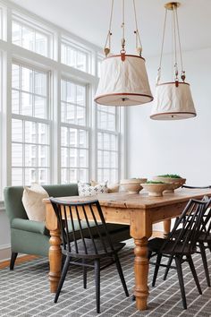 a dining room table and chairs with hanging lights above it in front of large windows