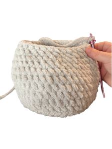 a hand holding a white knitted pouch