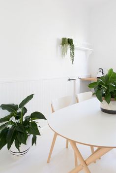 a white table with two potted plants sitting on it's sides next to a wooden chair