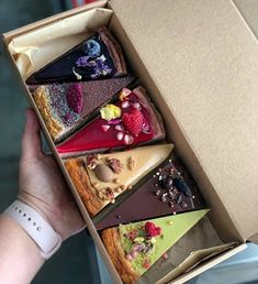 a person is holding an open box with different desserts in it