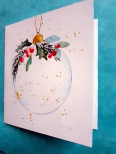 a white card with holly and berries on it sitting on a blue surface next to a pair of scissors