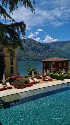 an outdoor swimming pool with chaise lounges and mountains in the background