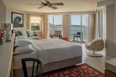 a bedroom with a bed, chair and ceiling fan in front of a balcony overlooking the water